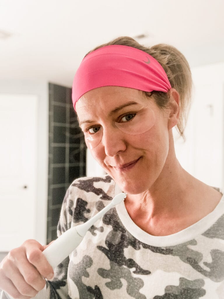 a woman holding a toothbrush with eye patches on 