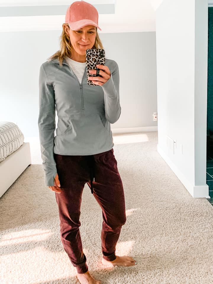 a woman in plum colored joggers, gray 1/2 zip pullover, and a pink hat