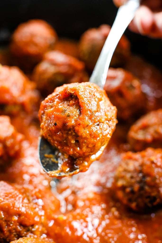 a vegan meatball on a spoon with a pan of meatballs in sauce in the background