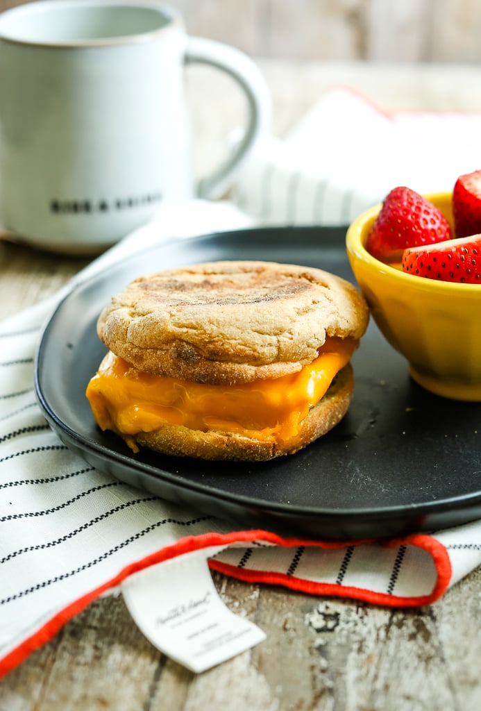 a breakfast sandwich on an English muffin with melted cheese and a small bowl of strawberries