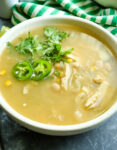 soup with cilantro and jalepeno peppers on top in a white bowl wit a green and white striped napkin