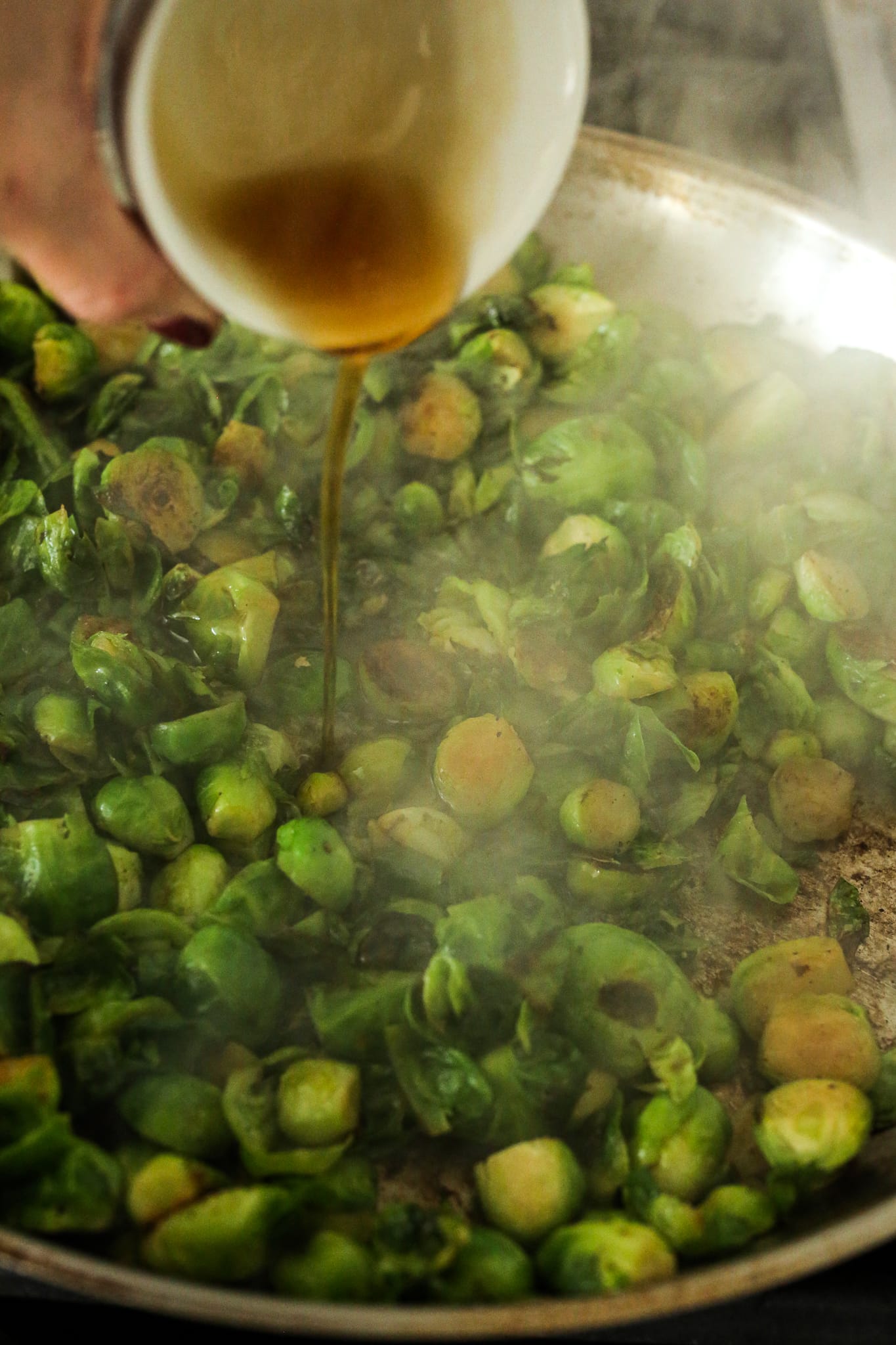 pouring maple syrup over hot brussels sprouts in a pan