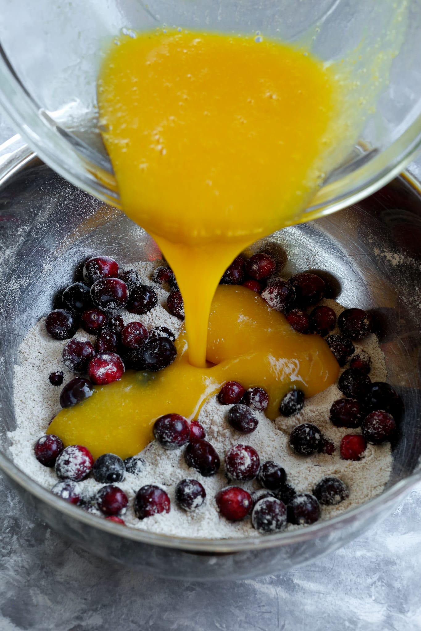 pouring a yellowish orange liquid into the cranberries and flour