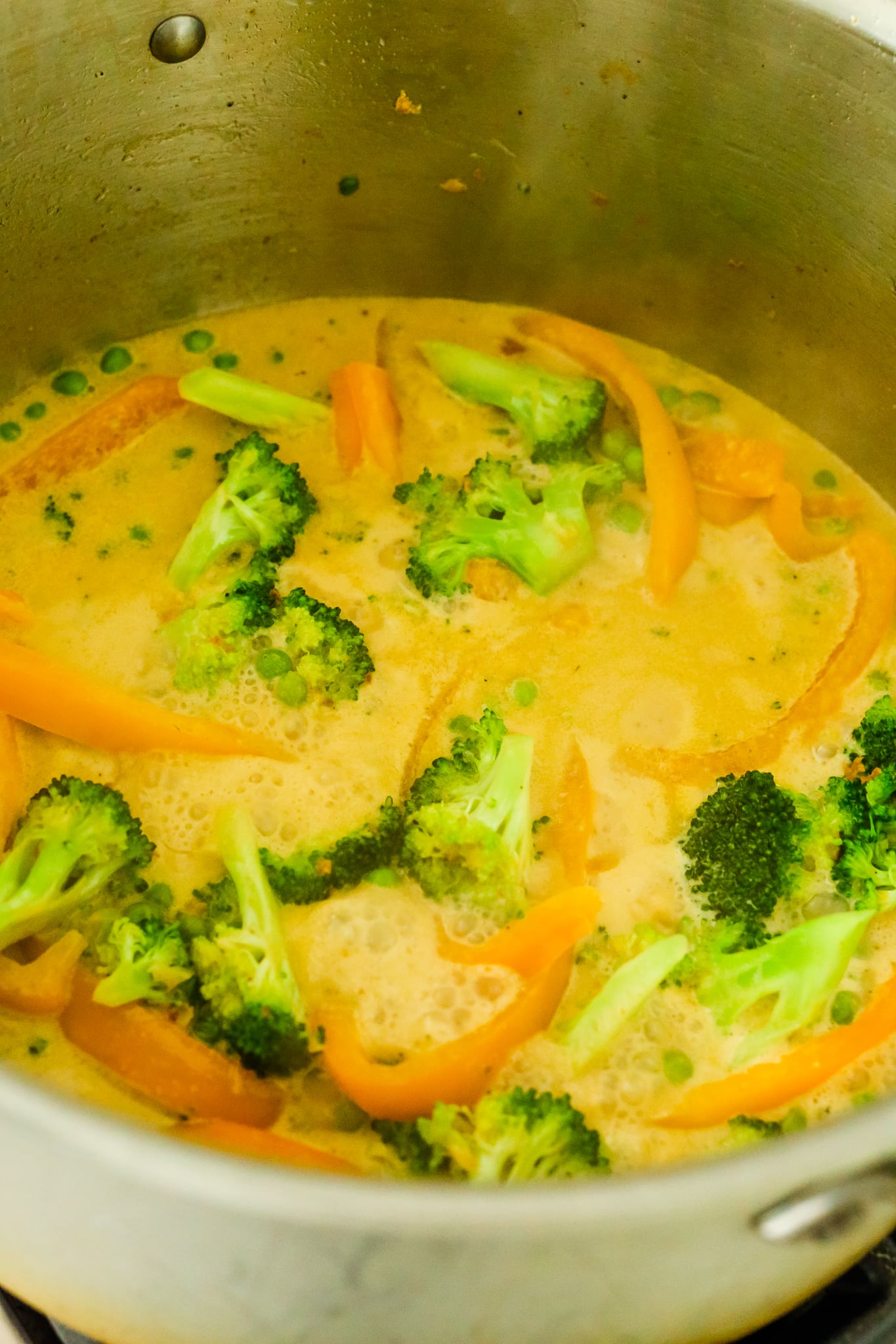 broccoli, orange bell pepper, and peas in a large pot with coconut curry sauce