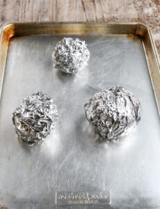 three tin foil balls on a rimmed baking sheet