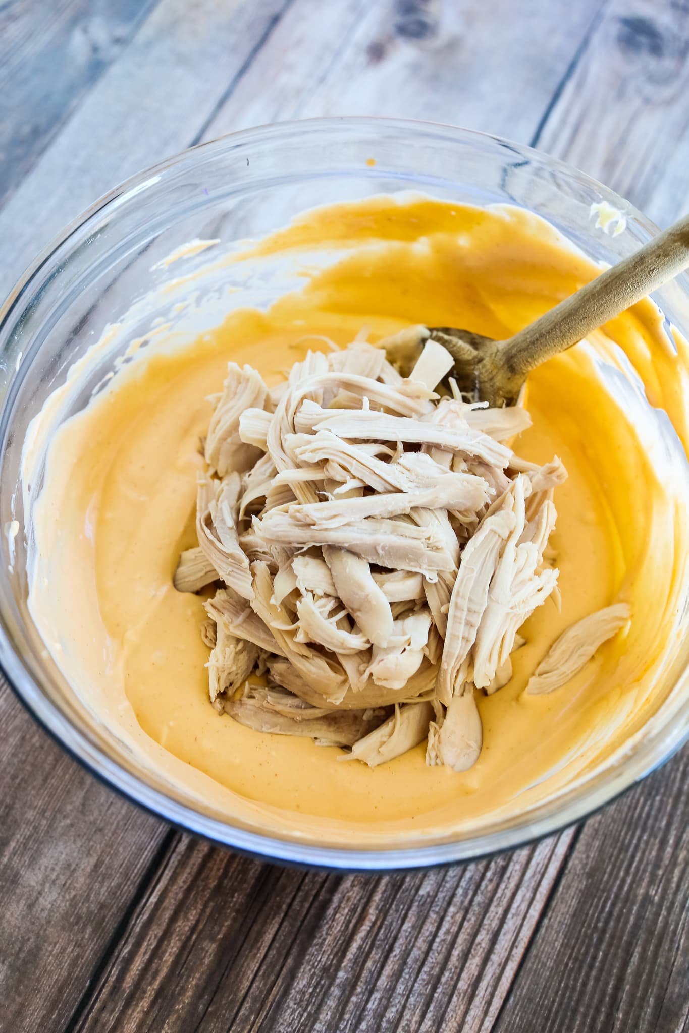 a clear bowl with a orange creamy mixture and chicken being stirred in