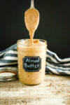 a mason jar labeled Almond Butter with a spoon and almond butter dripping from the spoon