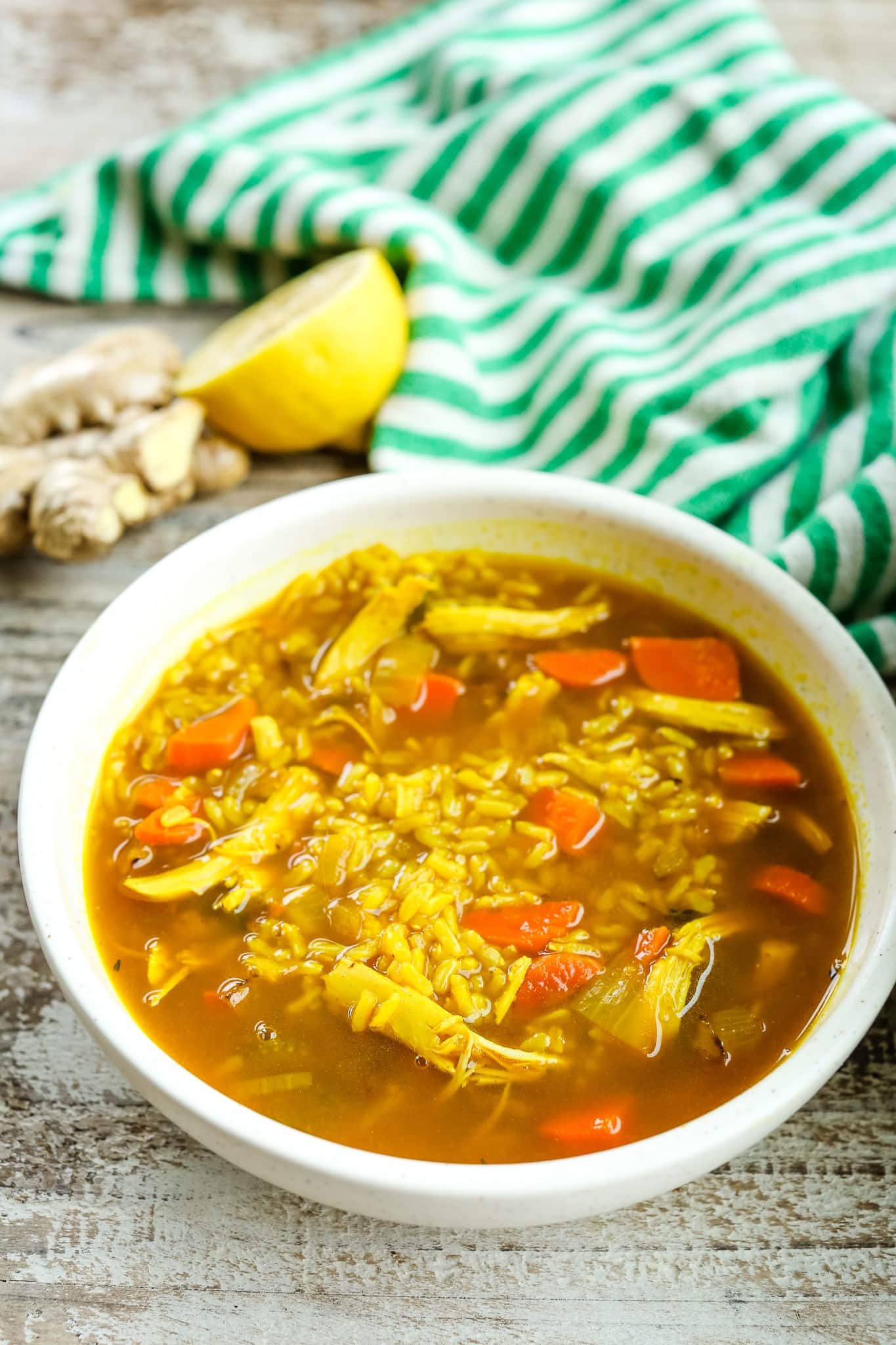 a bowl of soup pwith fresh ginger and lemon in the background and a green and white striped napkin