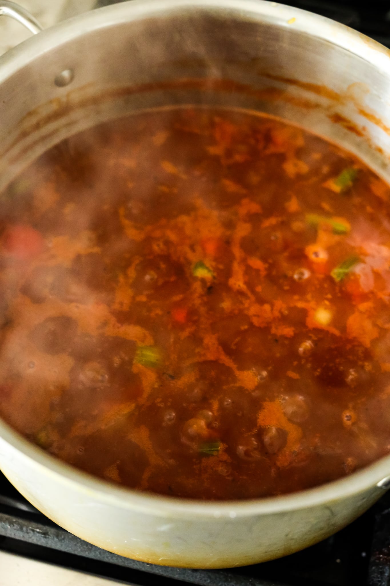 tomato based soup with black beans and vegetables in a soup pot simmering