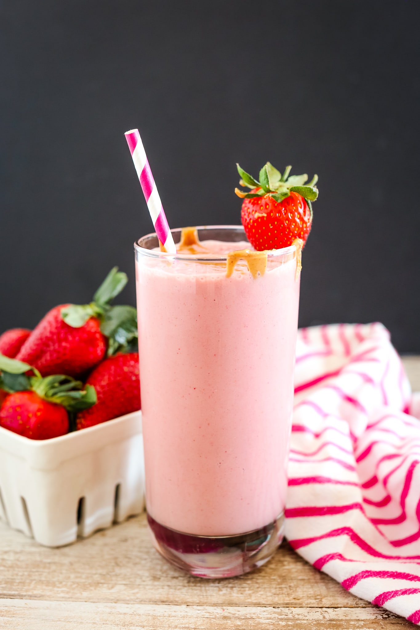 Strawberry Peanut Butter Smoothie recipe in a tall glass with a red and and white striped straw and a strawberry garnish