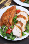 a chicken breast on a plate with salad cut into slices