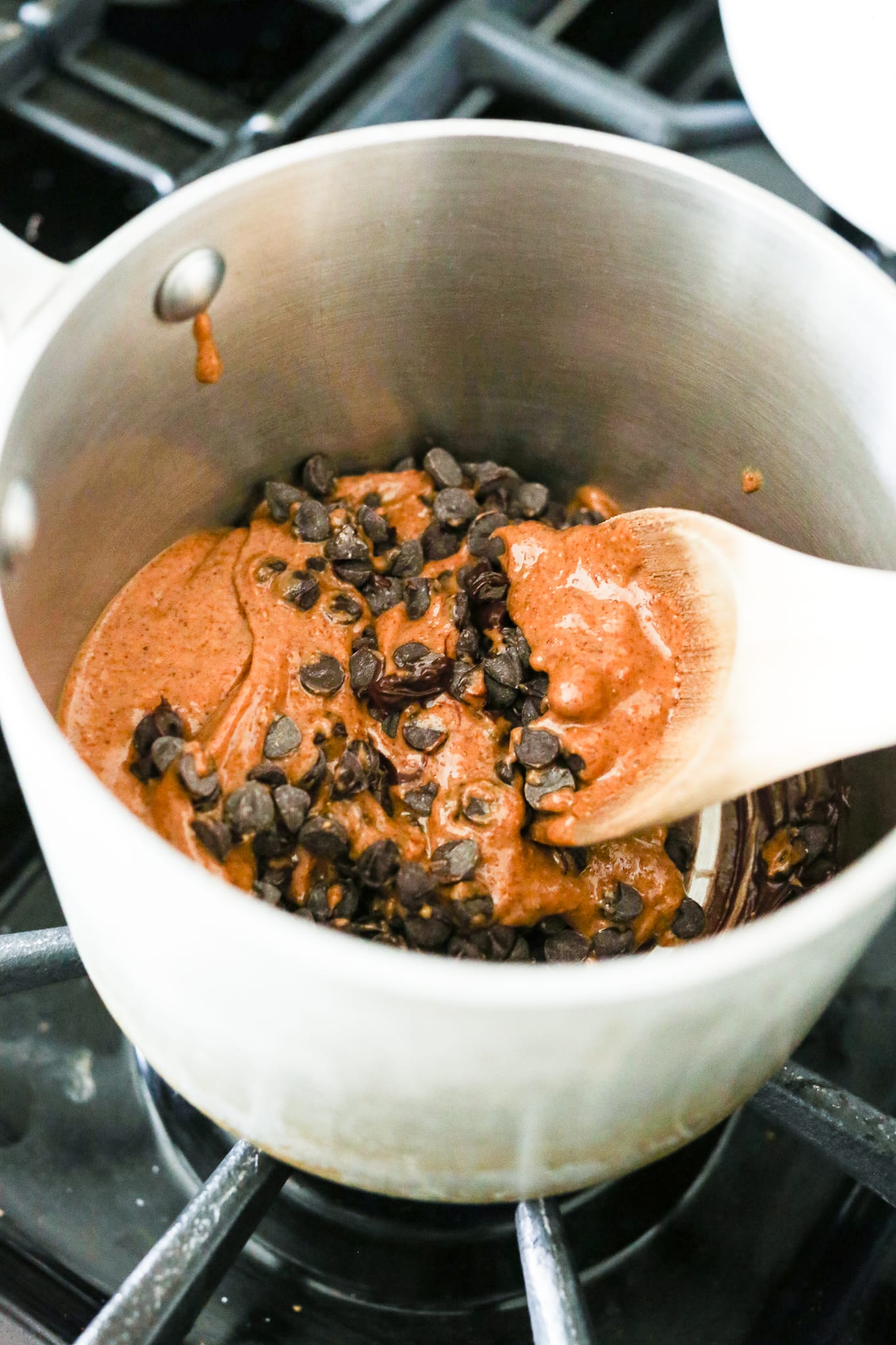 combining chocolate chips and almond butter in a saucepan with a wooden spoon