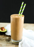 Cacao Smoothie recipe with 2 green straws and an avocado in the background