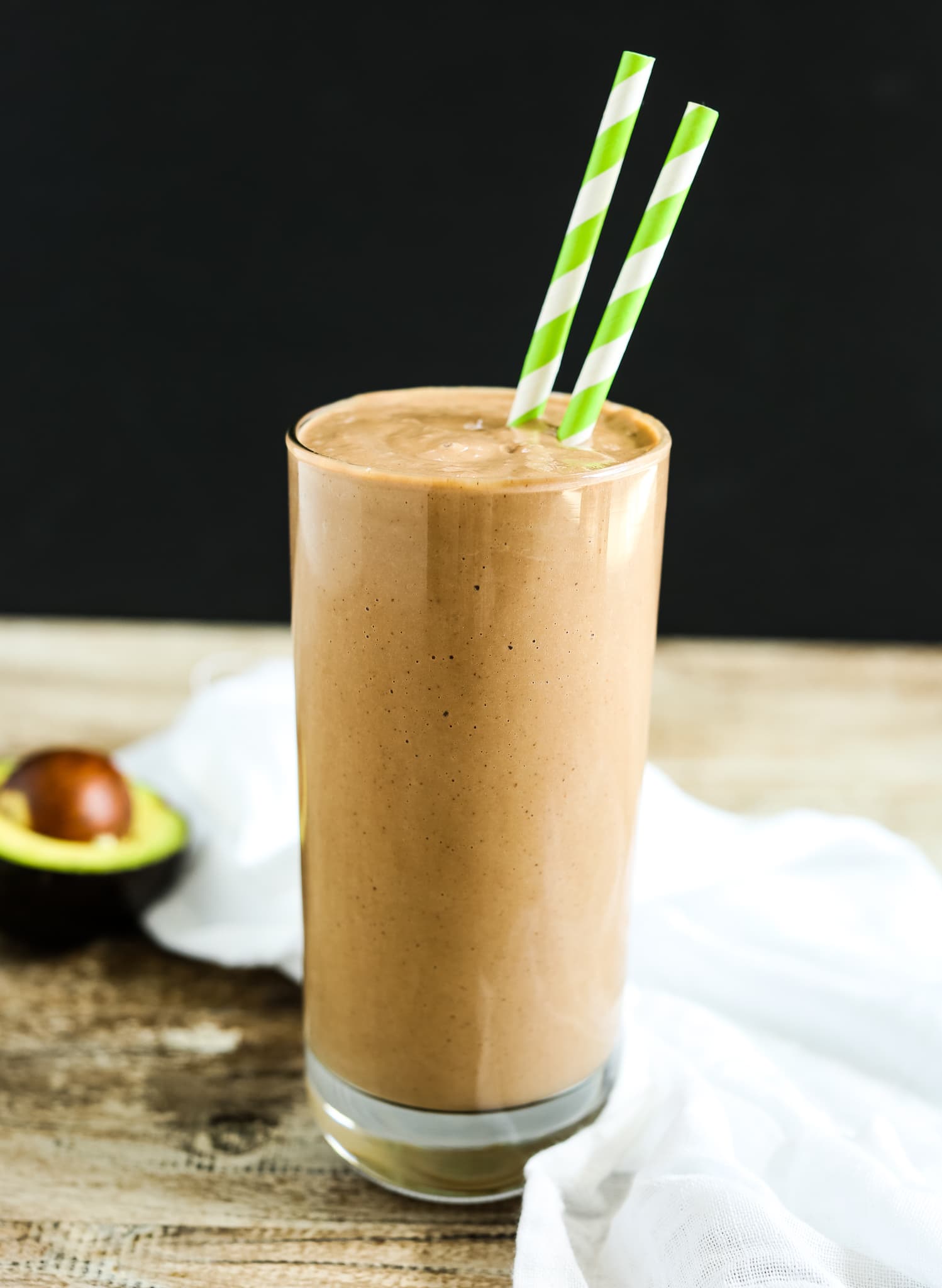 Cacao Smoothie recipe with 2 green straws and an avocado in the background