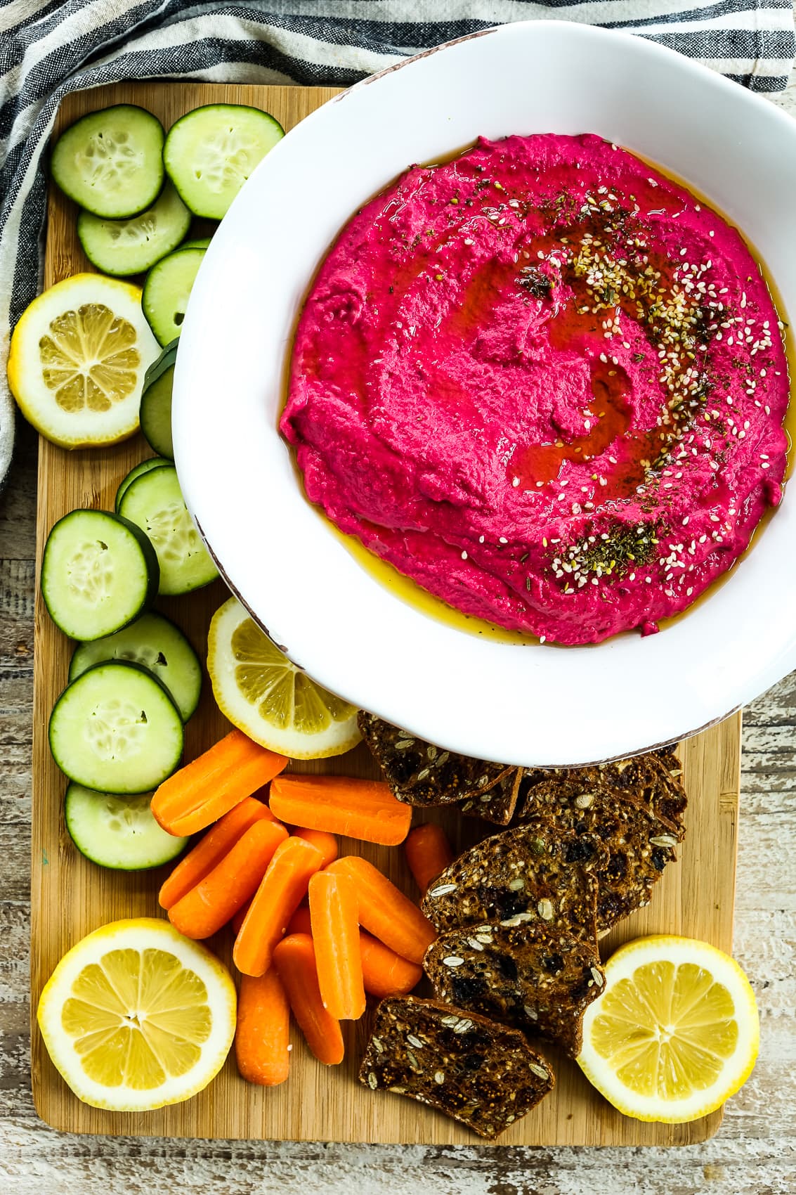 overhead shot of vibrant pink hummus in a bowl with carrots, cucumbers, and crackers