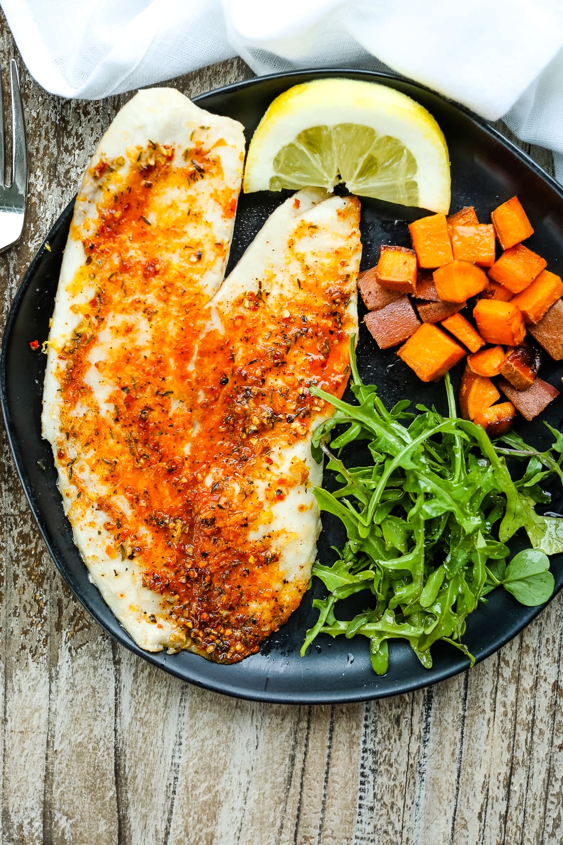 overhead shot of air fryer tilapia recipe on a plate with greens, lemon, and sweet potato