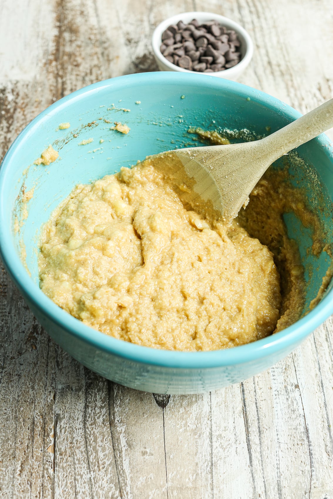 stirring the muffin batter with a wooden spoon in a turquoise bowl