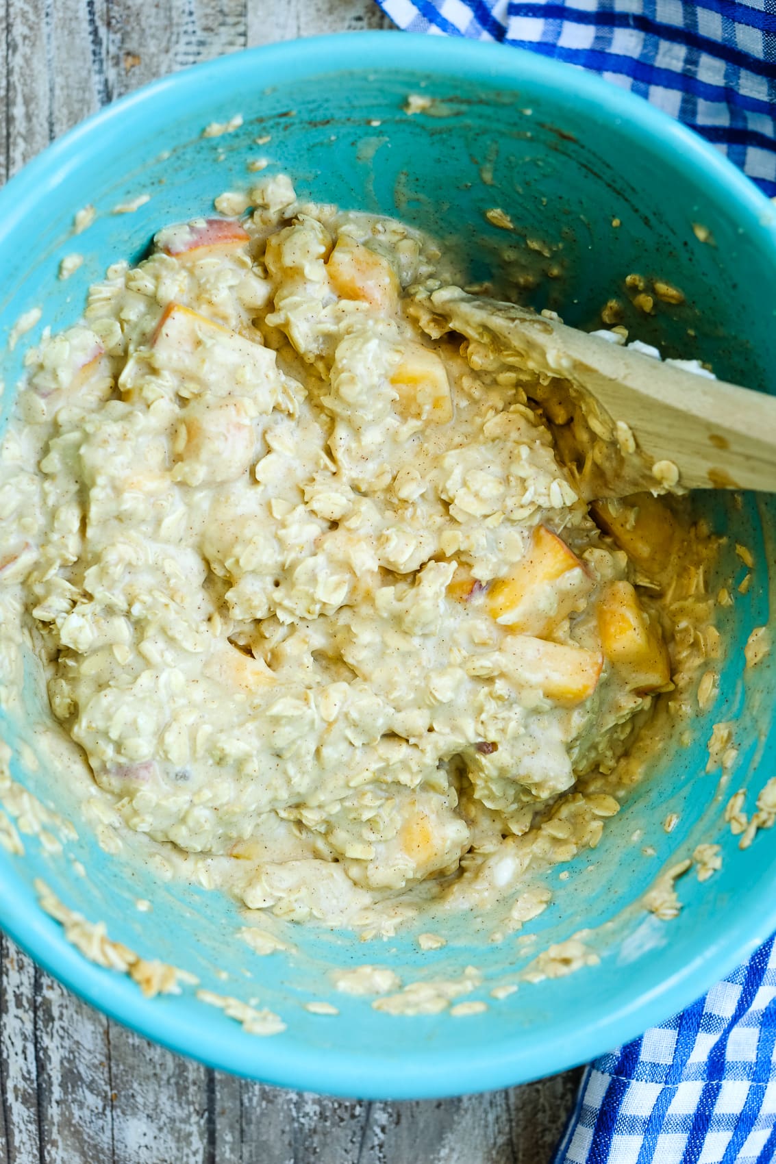 baked oatmeal batter with peach chunks in a blue bowl with a wooden spoon