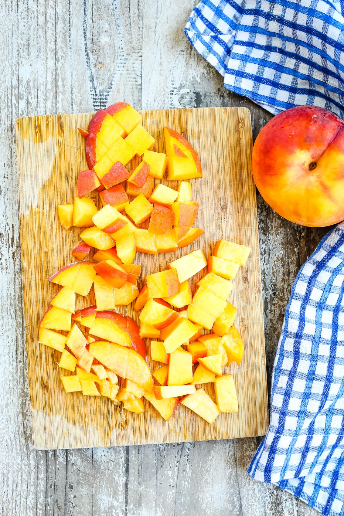 a whole peach next to a cutting board with a peach cut into pieces