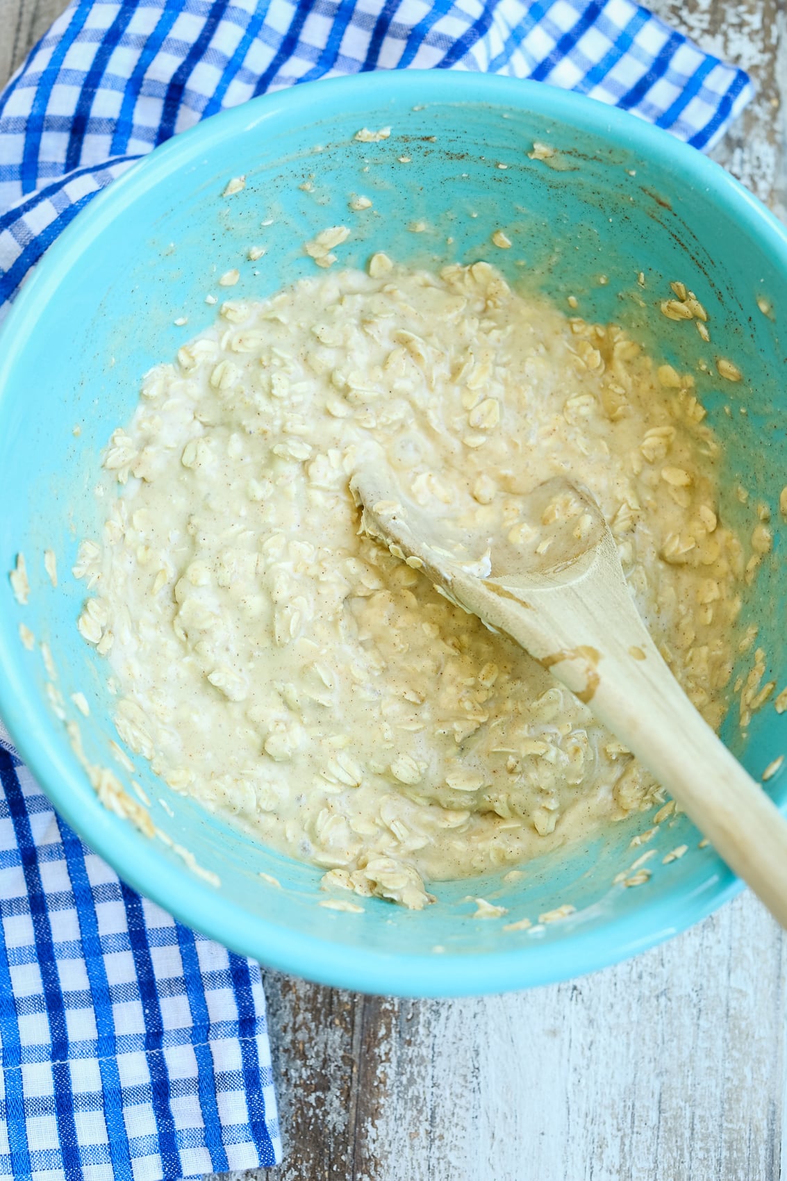 baked oatmeal batter in a blue bowl with a wooden spoon