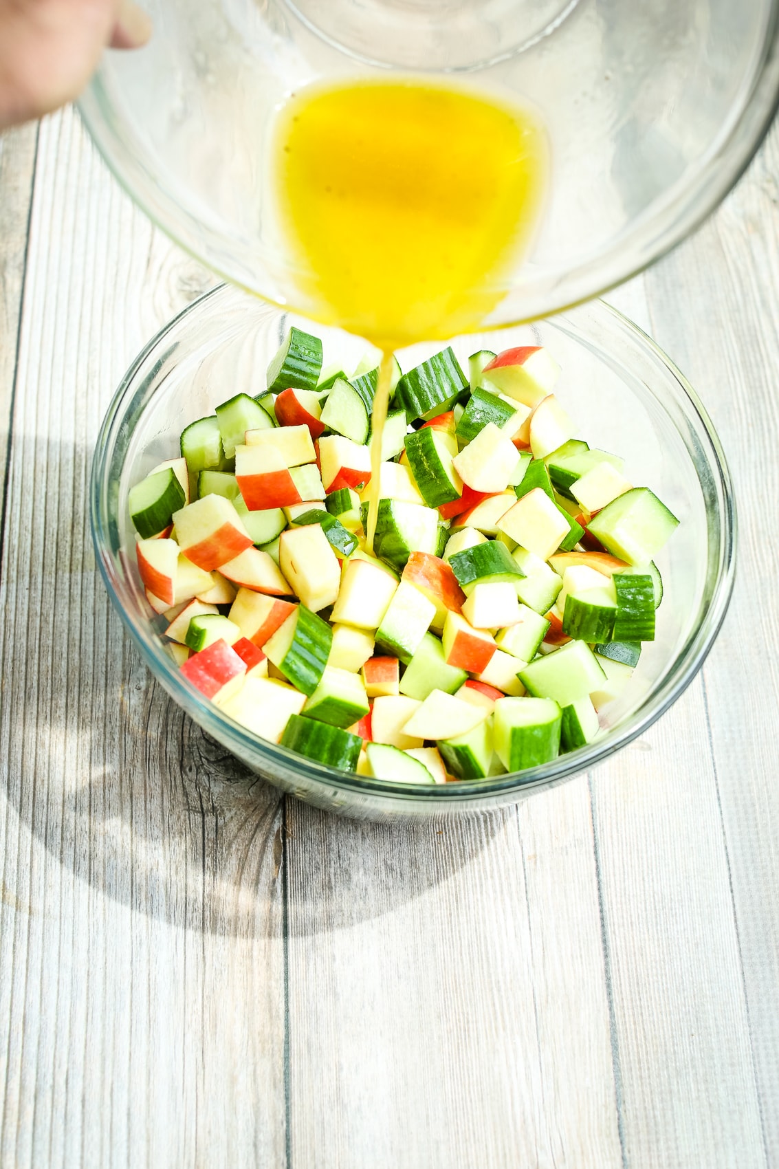 pouring dressing over cucumber and apples in a bowl