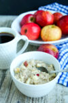 a bowl of oatmeal with a cup of coffee and a bowl of fresh apples in the background