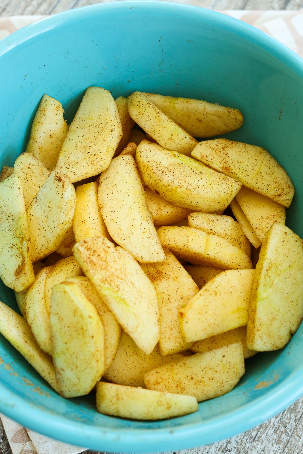 sliced apples coated with cinnamon in a turquoise blue bowl