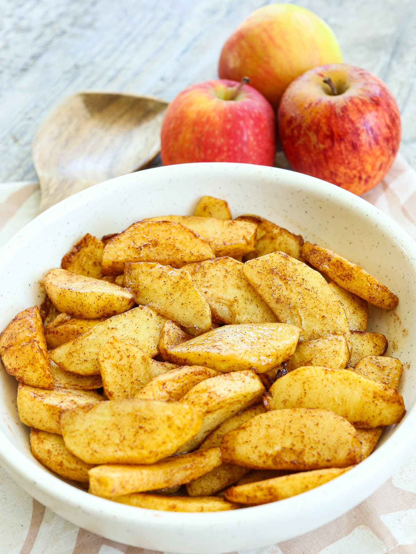 Air fryer apples in a bowl with fresh apples in the background