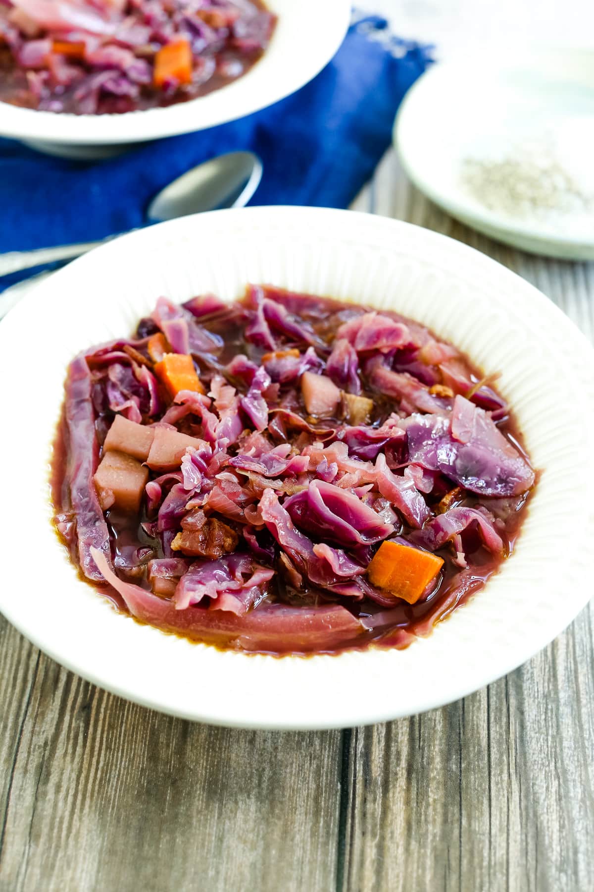 overhead shot of Red Cabbage Soup recipe in a white bowl with a navy napkin and spoon in the background
