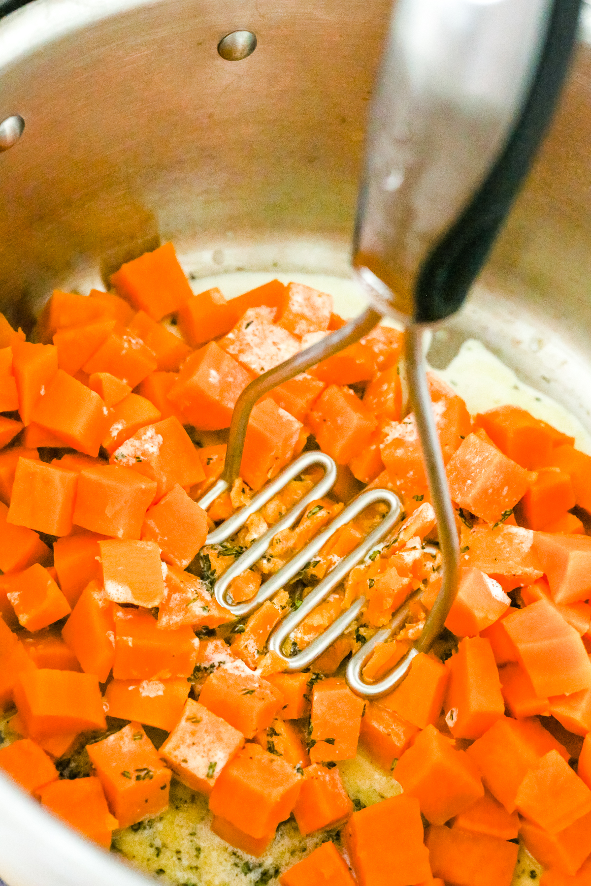using a potato masher to mash sweet potatoes