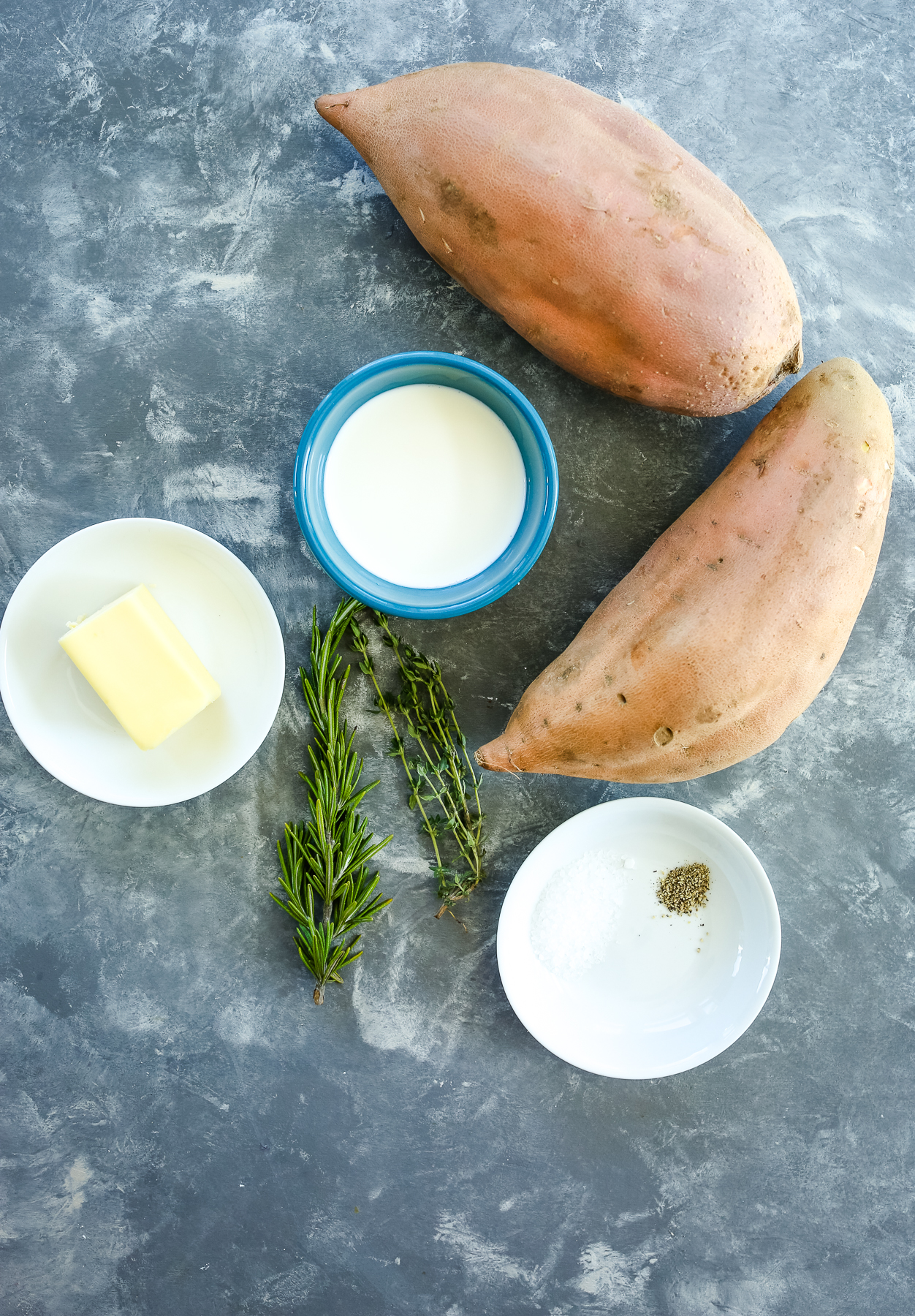 overhead shot of 2 sweet potatoes, fresh herbs, butter, salt, pepper, and half-and-half in a bowl