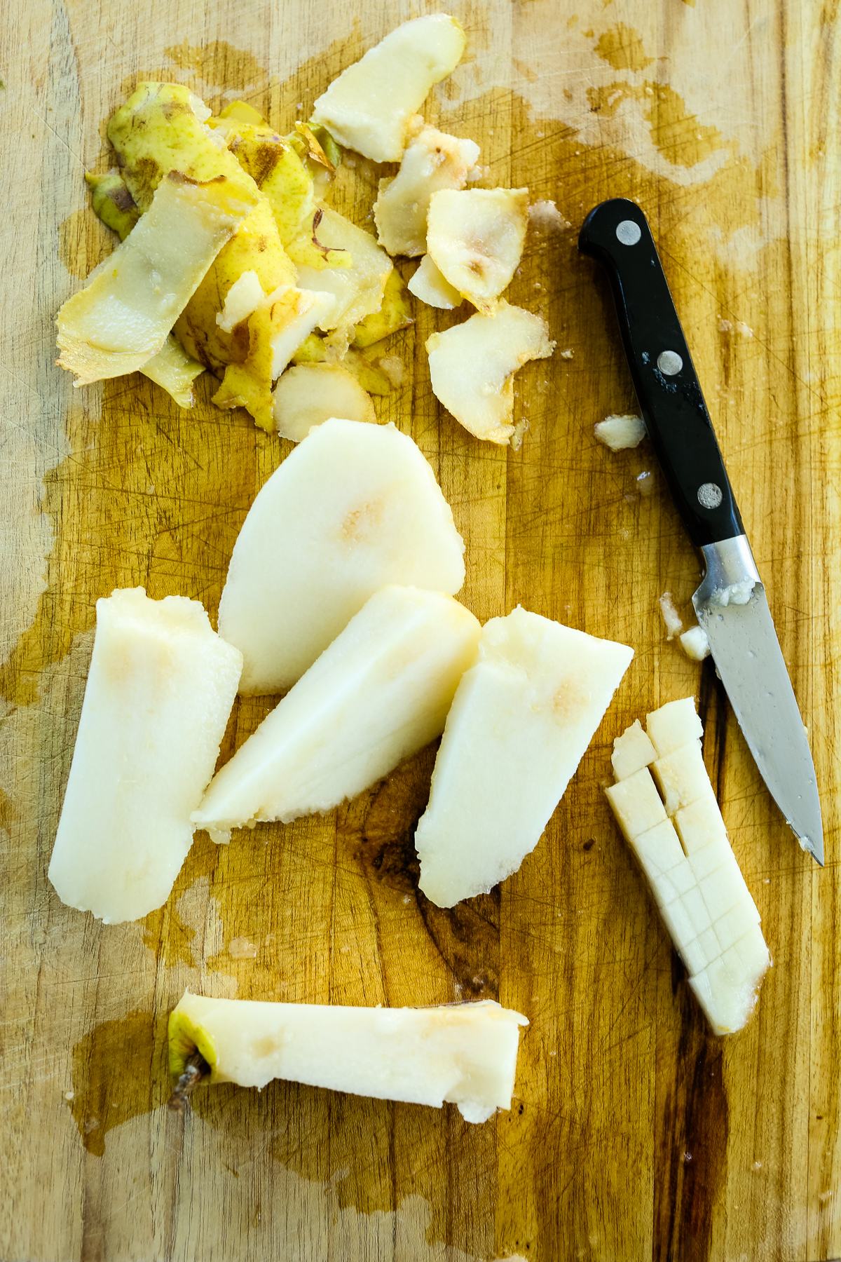 a cutting board with ripe pears that have been peeled and are cut into large chunks with a pairing knife on the side