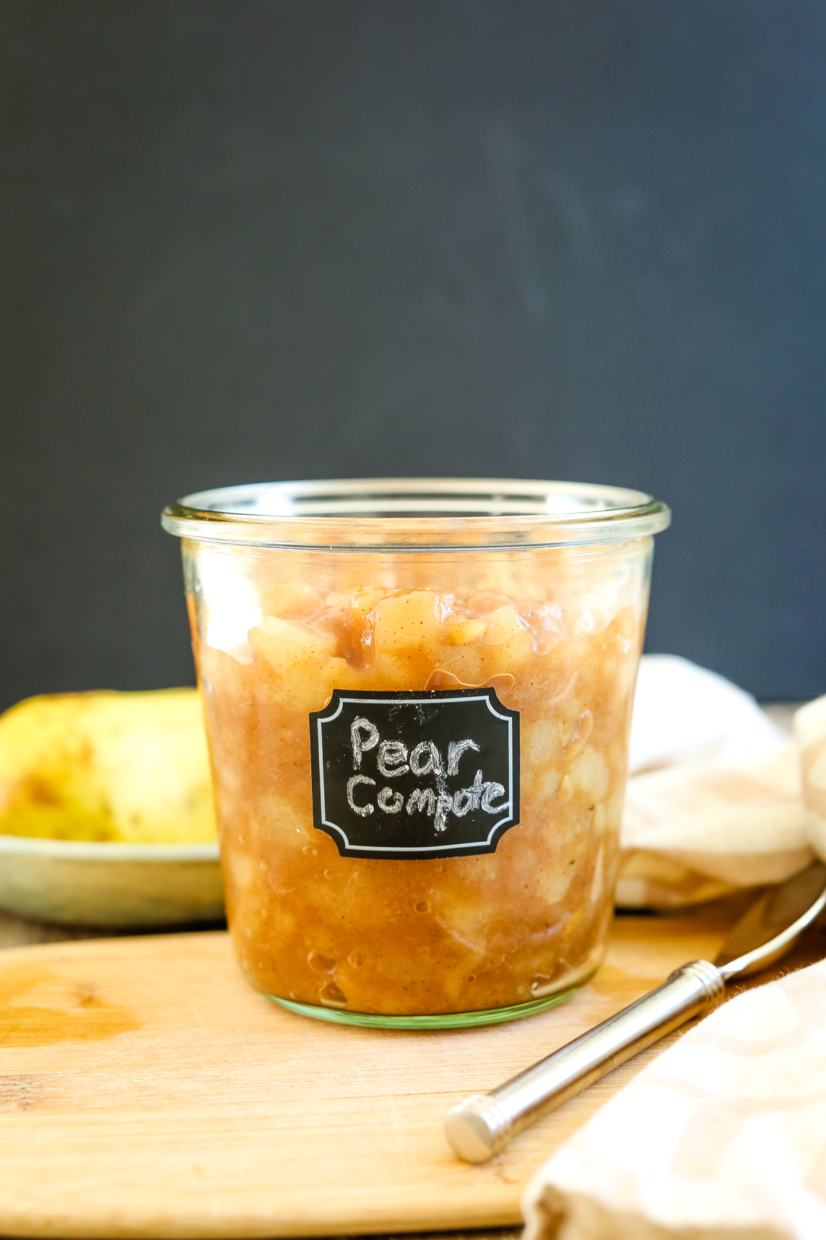 pear compote in a labeled glass jar with a fresh pear in background