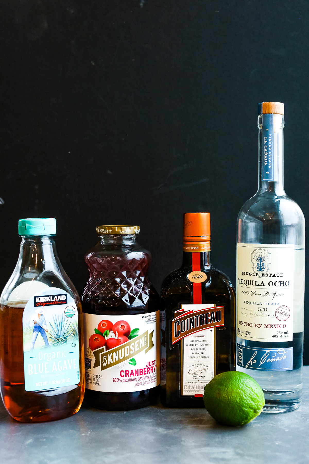 agave nectar, cranberry juice, cointreau, and tequila and a lime in a row