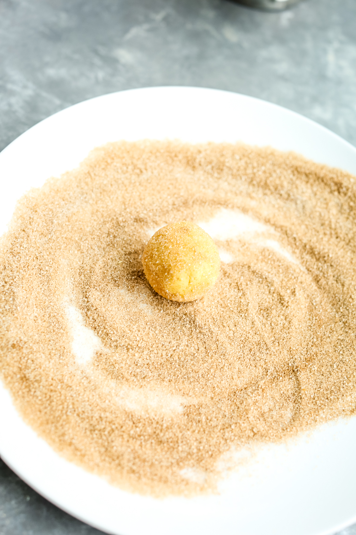 cinnamon sugar mixture on a plate with a dough ball being rolled