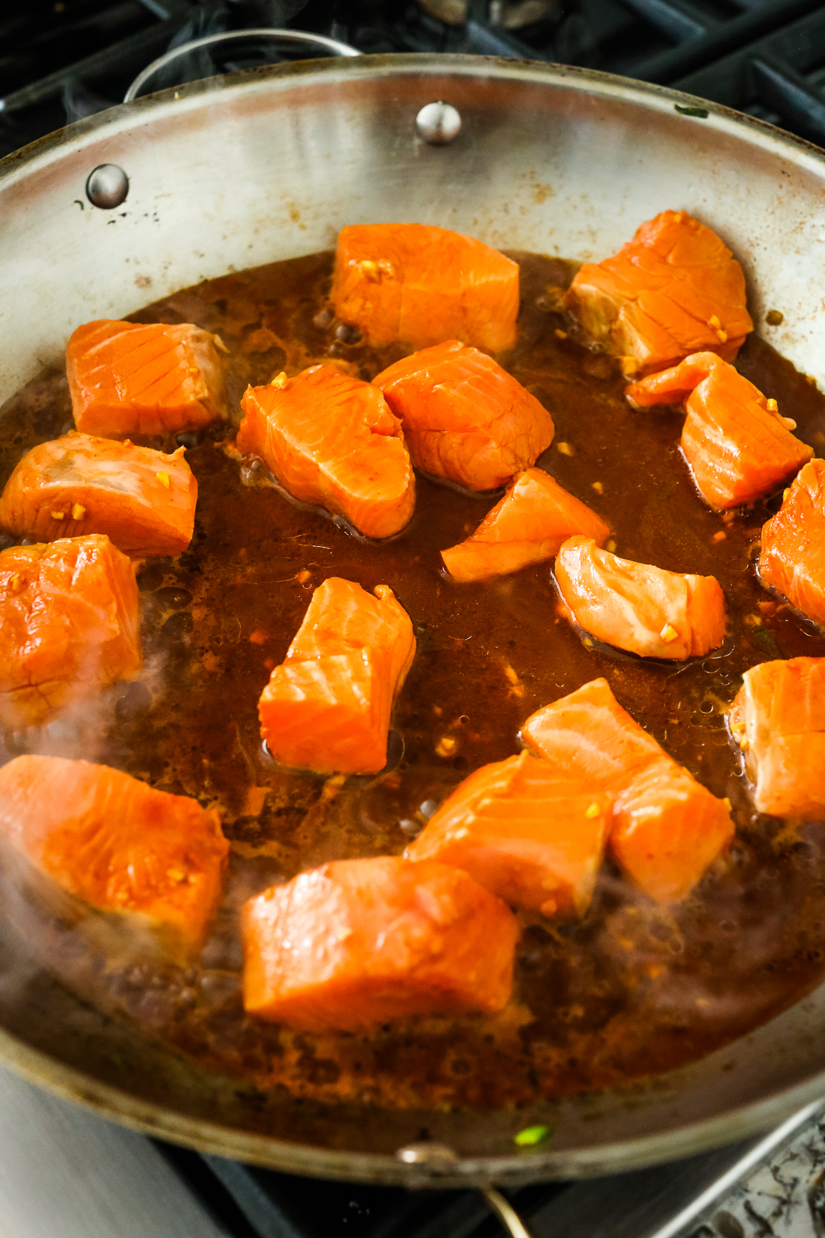 salmon pieces cooking in sauce in a large pan