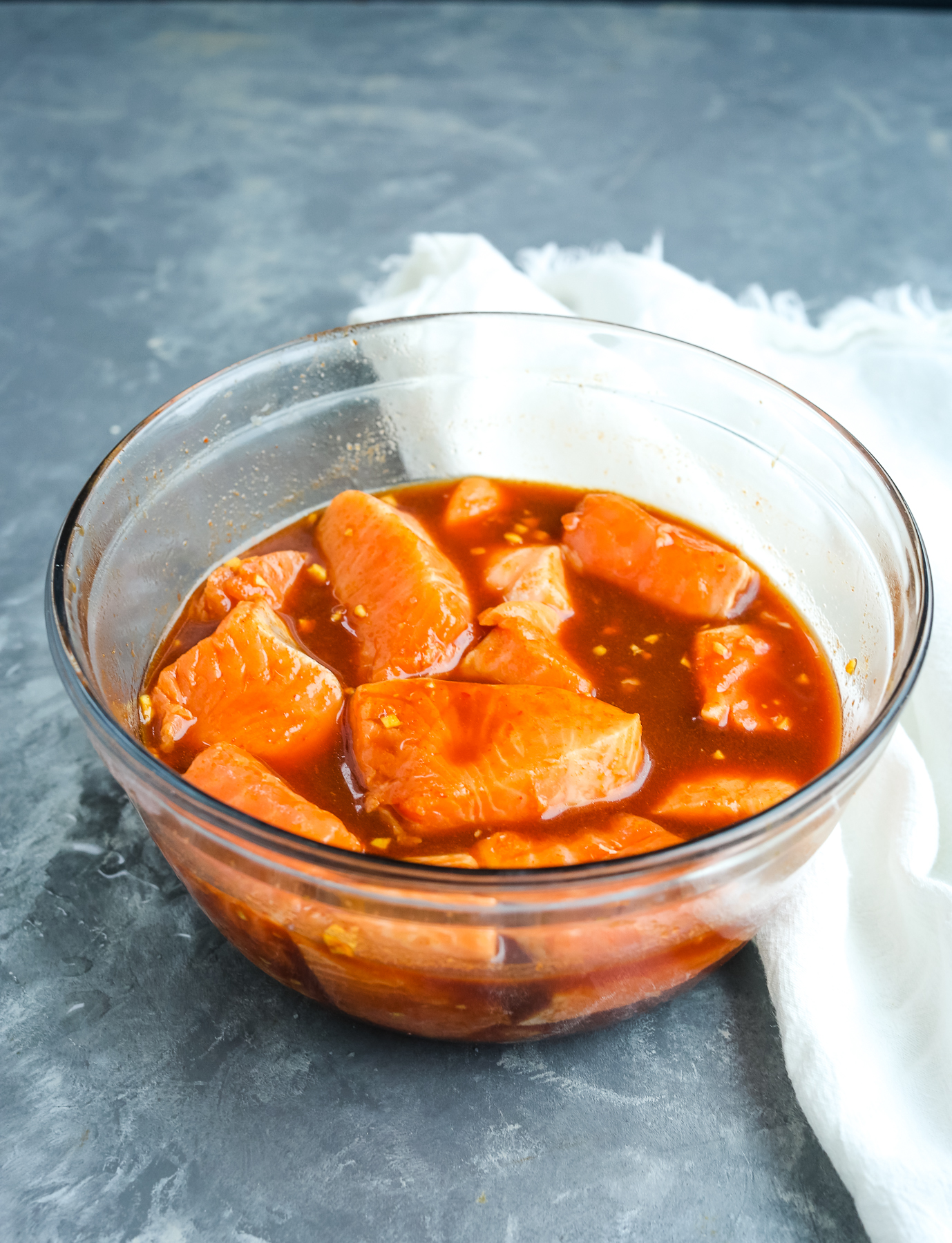 salmon pieces marinating in a glass bowl with brown liquid