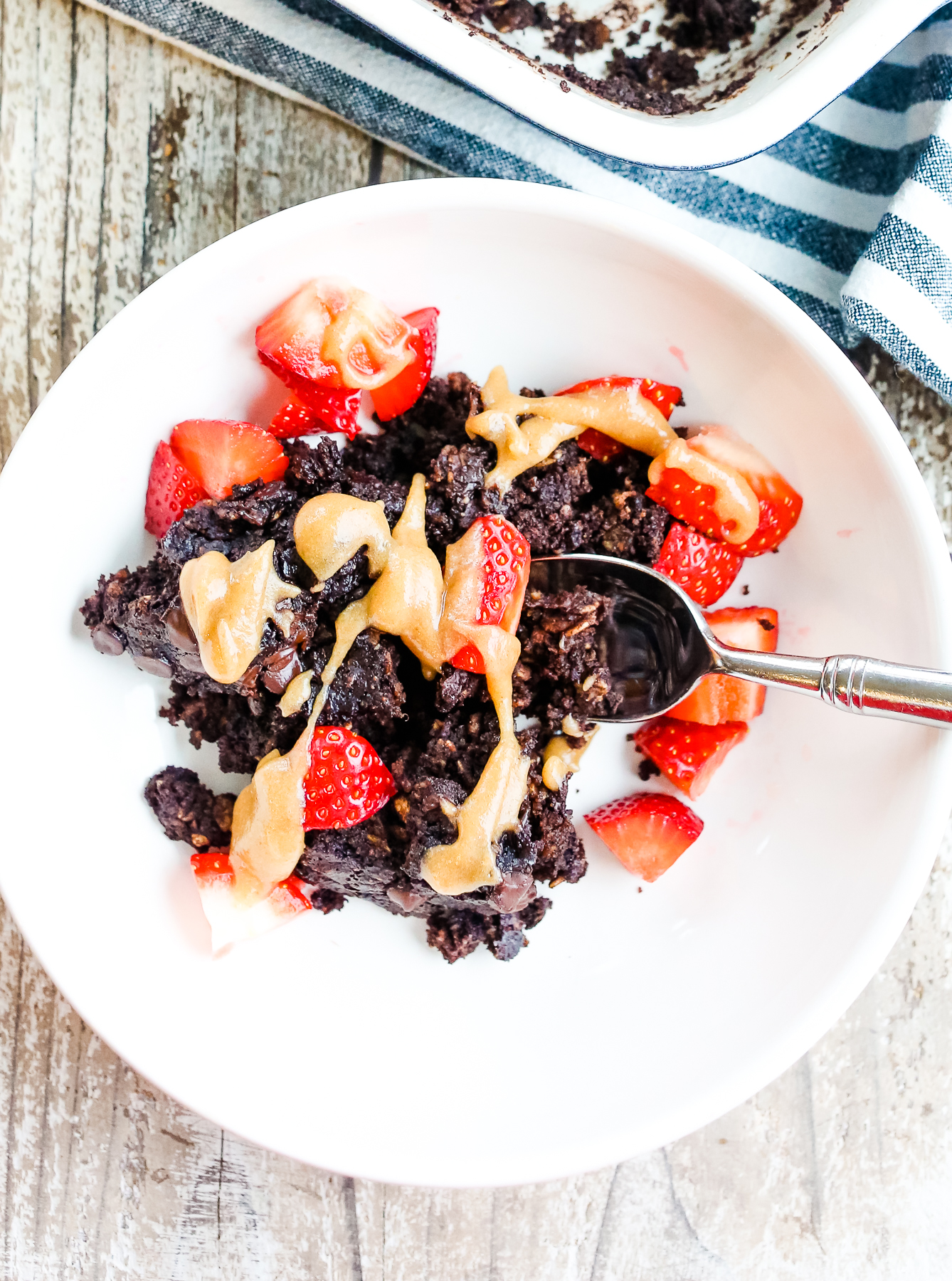 Chocolate Baked Oats in a white bowl with strawberries and a little caramel sauce on top
