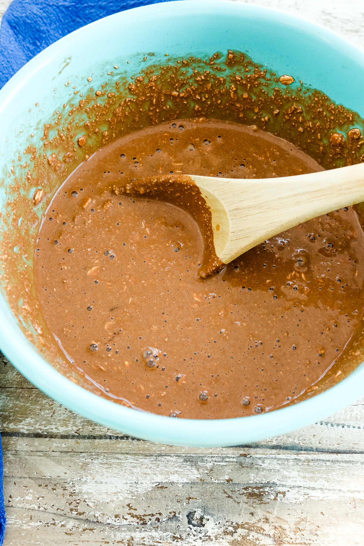 chocolately oats mixture in a turquoise bowl with a wooden spoon stirring it