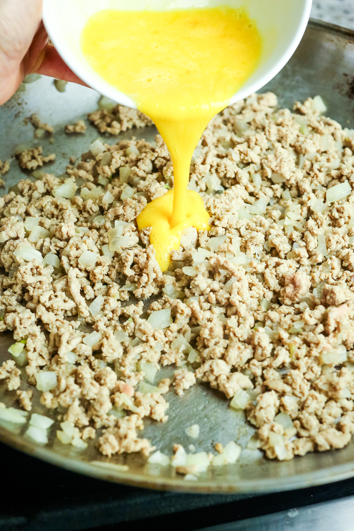 pouring whisked egg into turkey and onion mixture in a pan