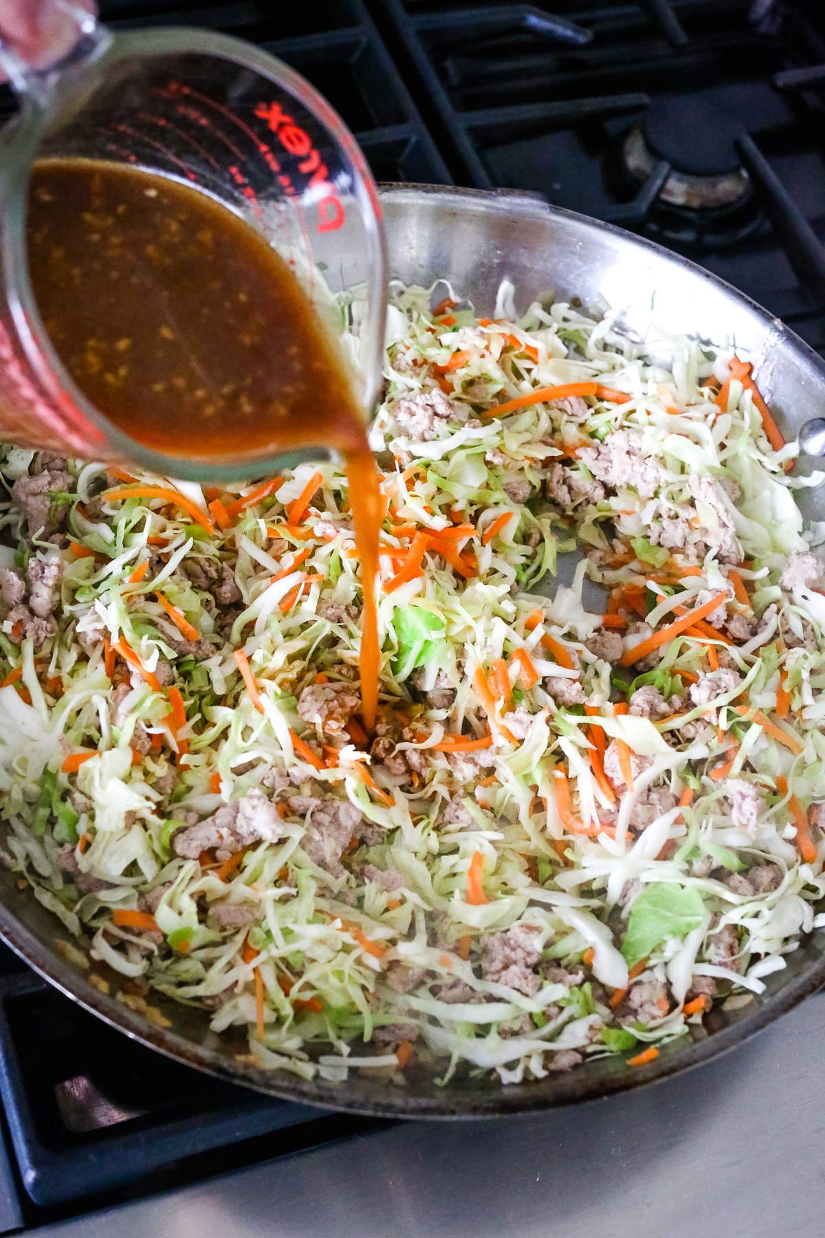pouring sauce into a large skillet with cole slaw mix and ground turkey