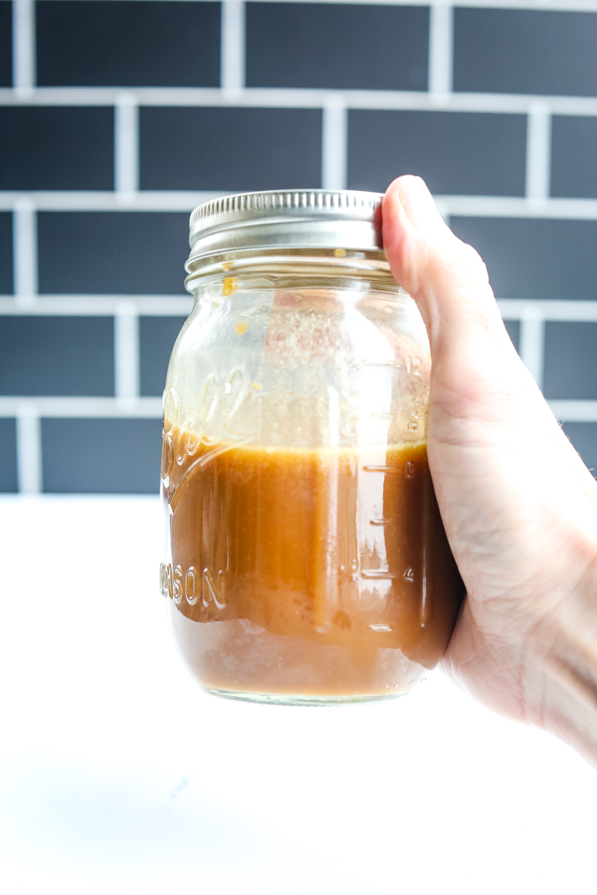 a jar with brown sauce and a hand shaking it