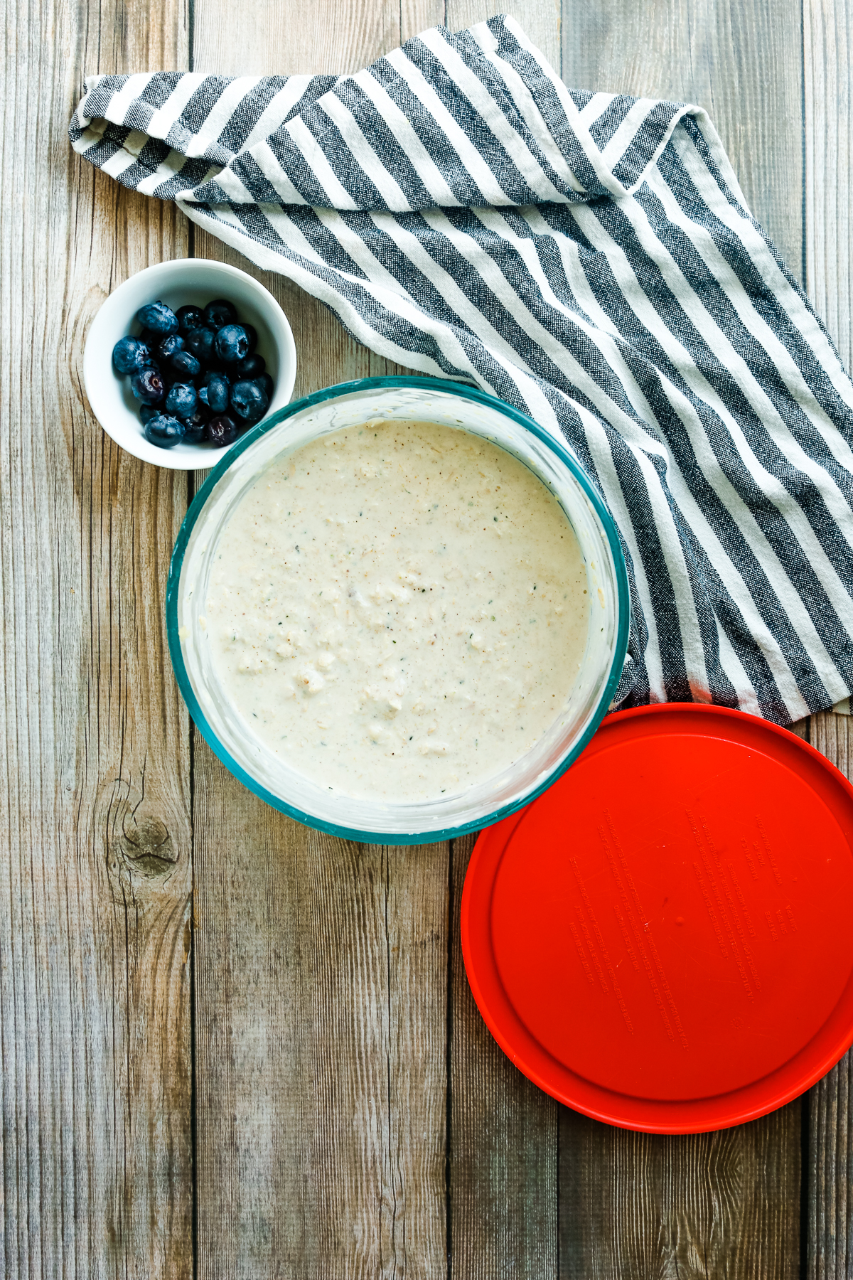 a bowl of blueberries next to a bowl of oats and a red plastic lid.