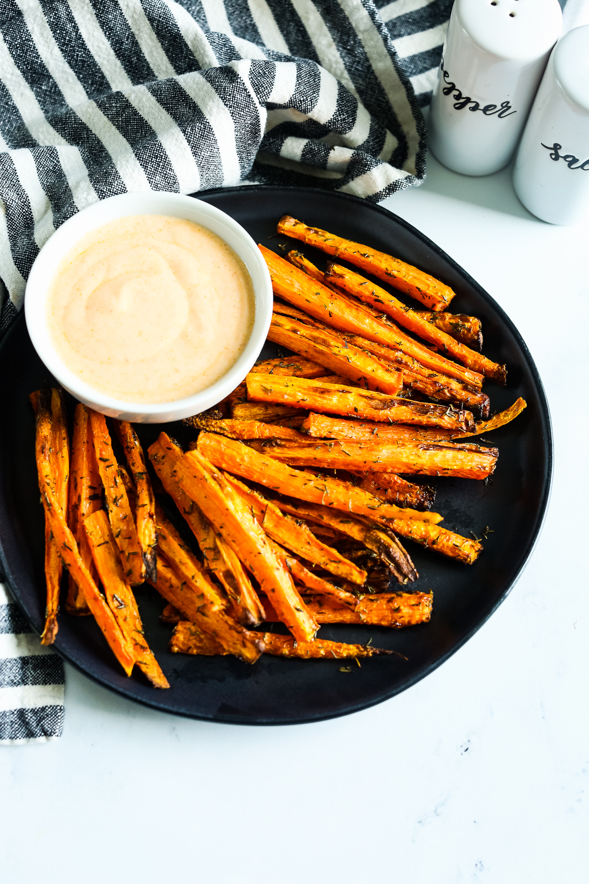 a black plate with carrots in a fry shape and a dipping sauce