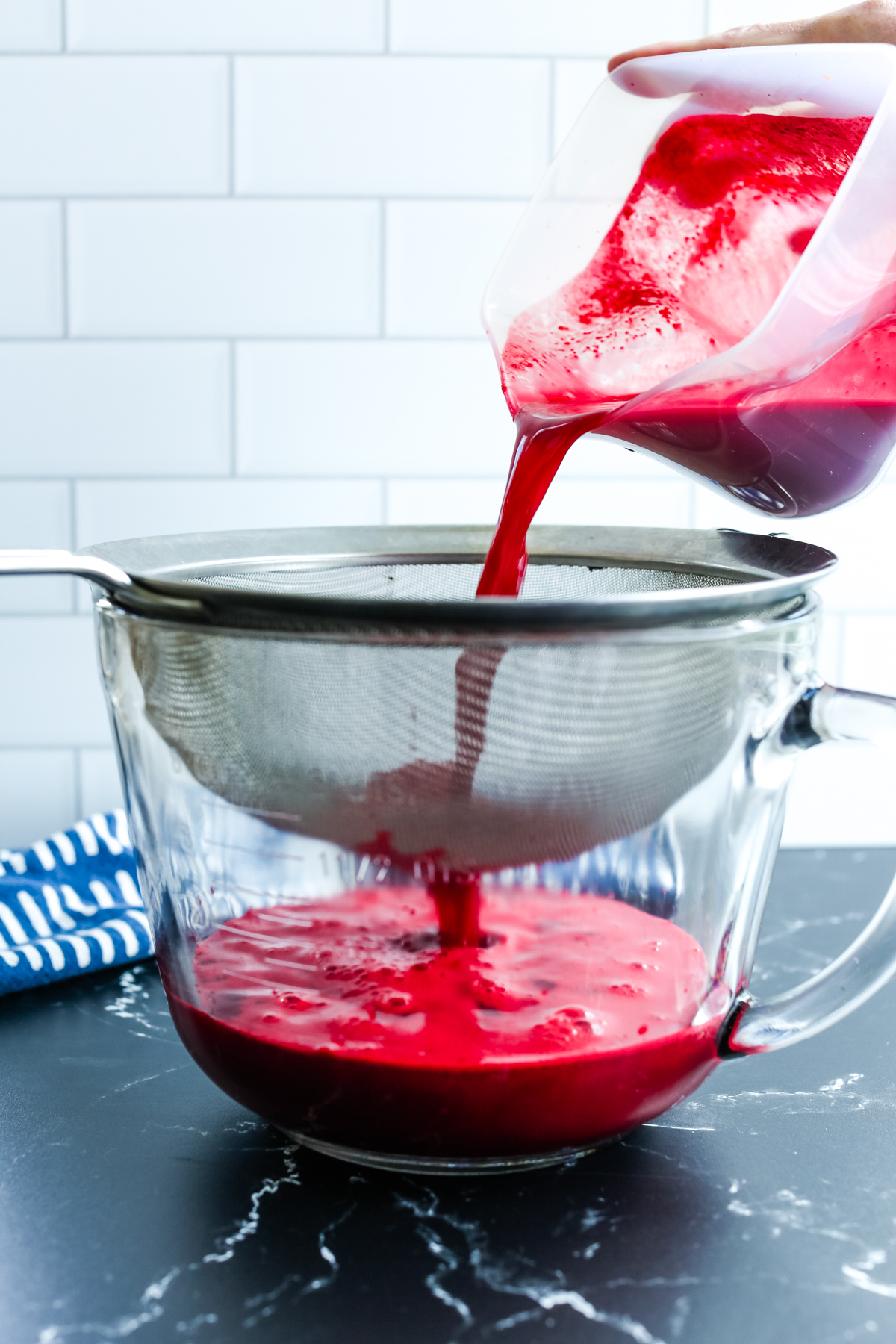 straining a vibrant red juice through a fine mesh sieve