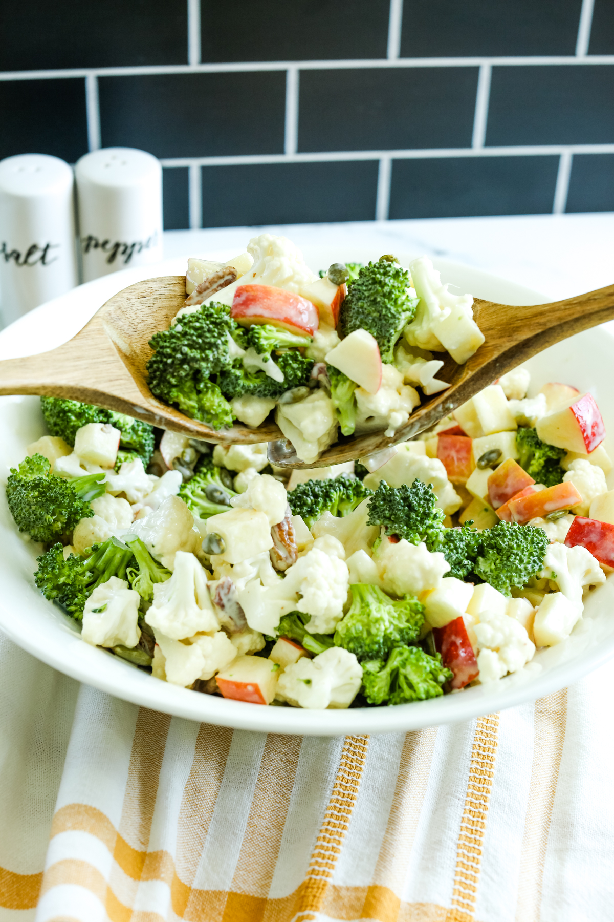 Broccoli Cauliflower Salad being served from a white bowl with 2 wooden spoons