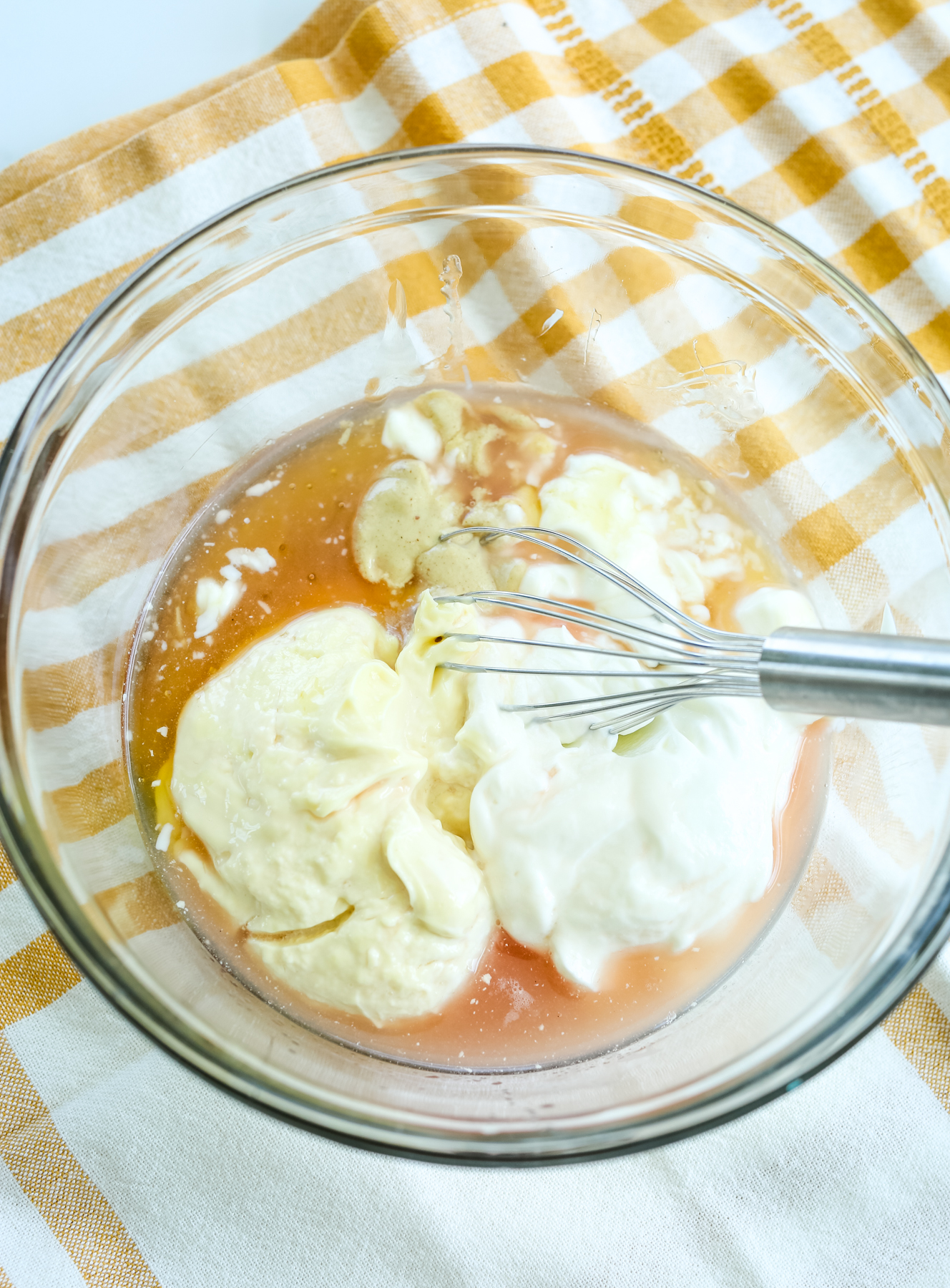 Mayonnaise, Greek yogurt, mustard, and honey in a glass bowl with a whisk