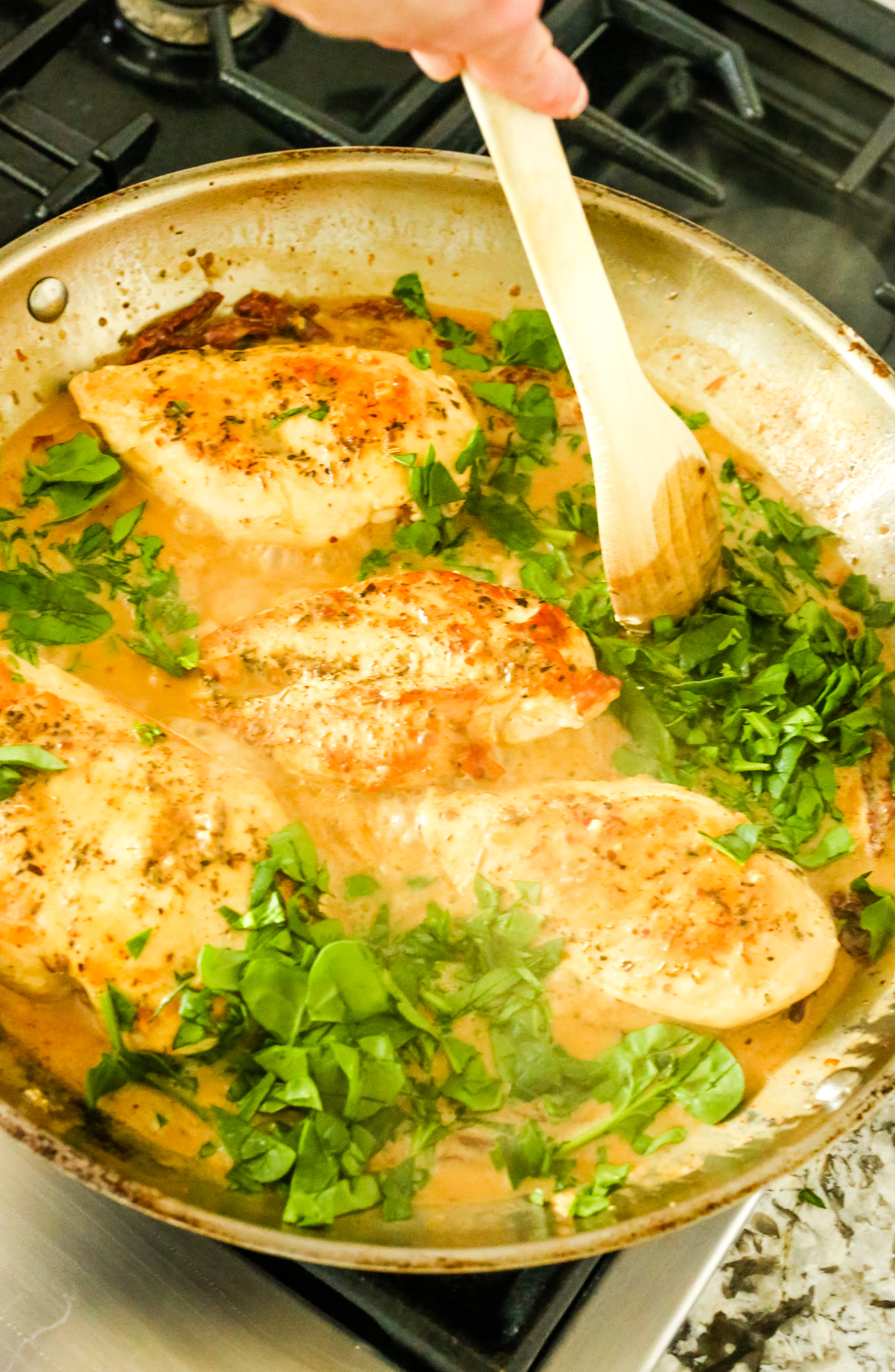 stirring spinach leaves into sauce with chicken breasts