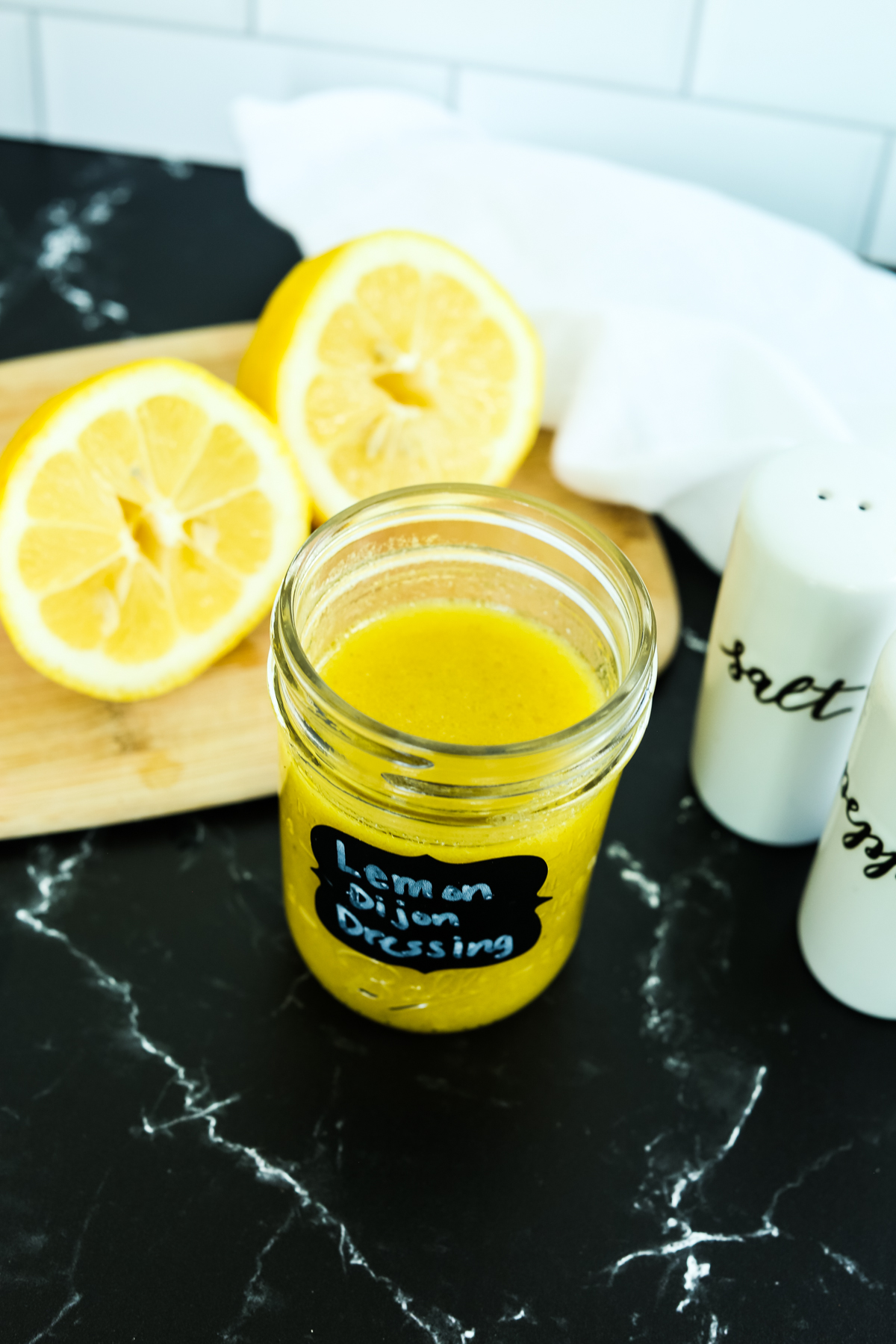 a yellow hued dressing in a jar with lemons in the background 