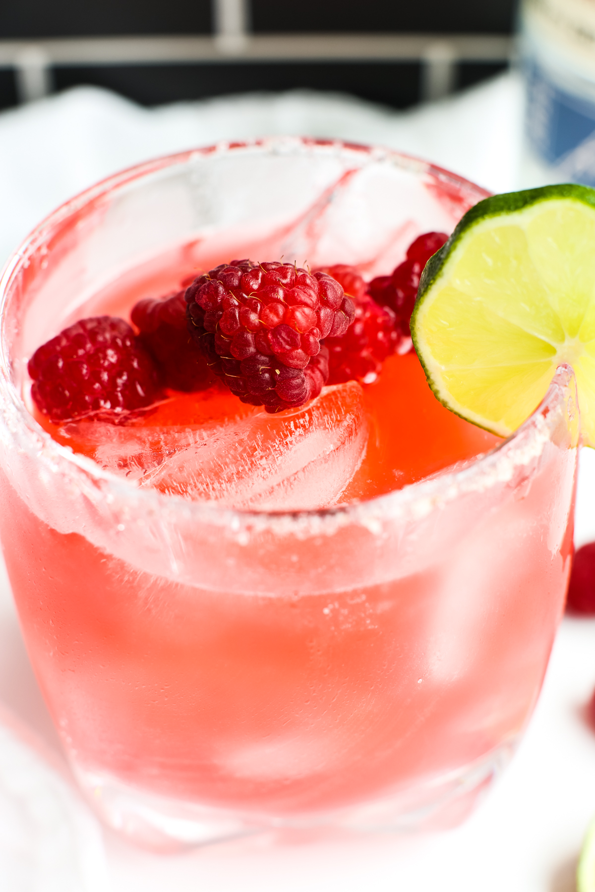 A pinkish red cocktail with raspberries and a lime garnish